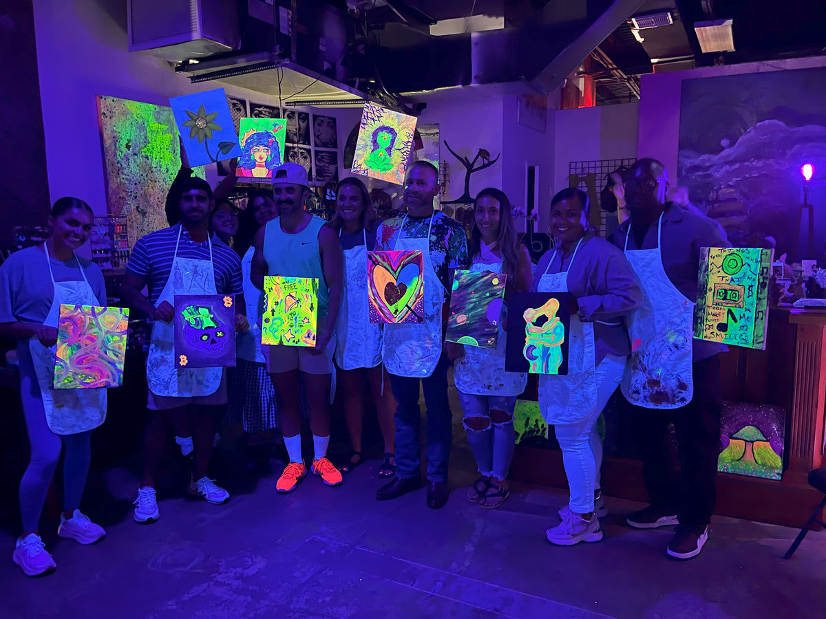 Group of guests proudly holding their neon paintings after a BYOB Neon Nights paint and sip session in Tampa.