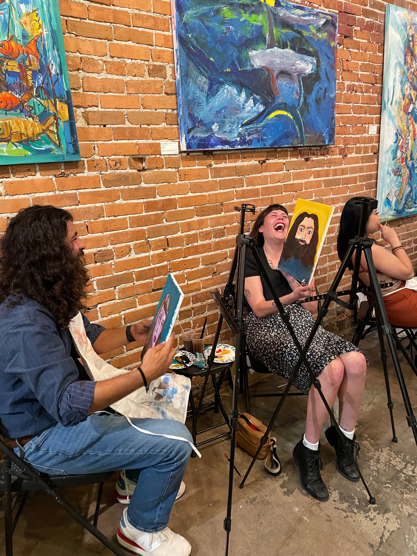 Couple laughing while showing each other the portrait paintings they created during a paint-each-other sip and paint session in Tampa.