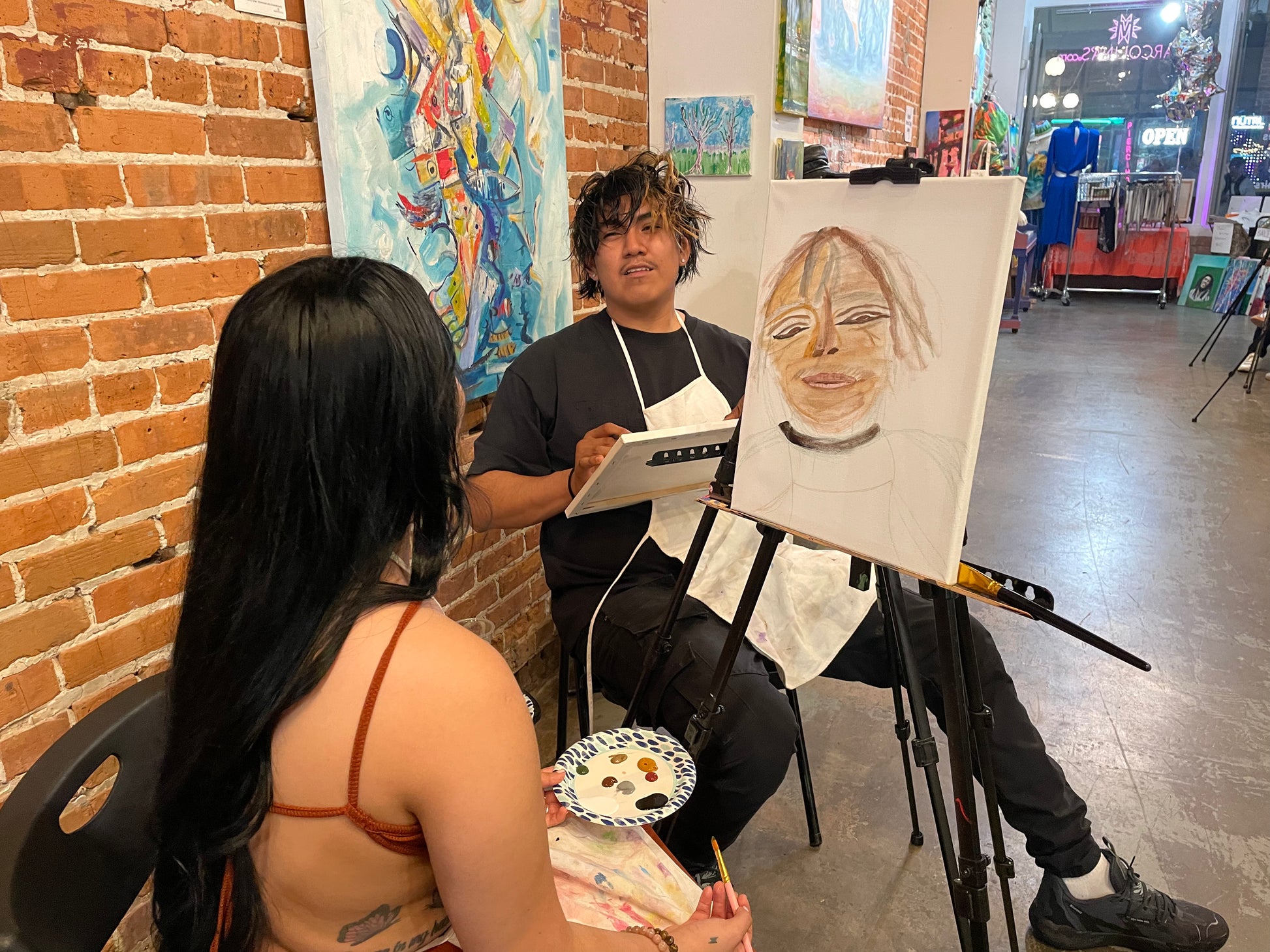 Couple painting each other’s portraits during the You Paint Me, I Paint You sip and paint experience.