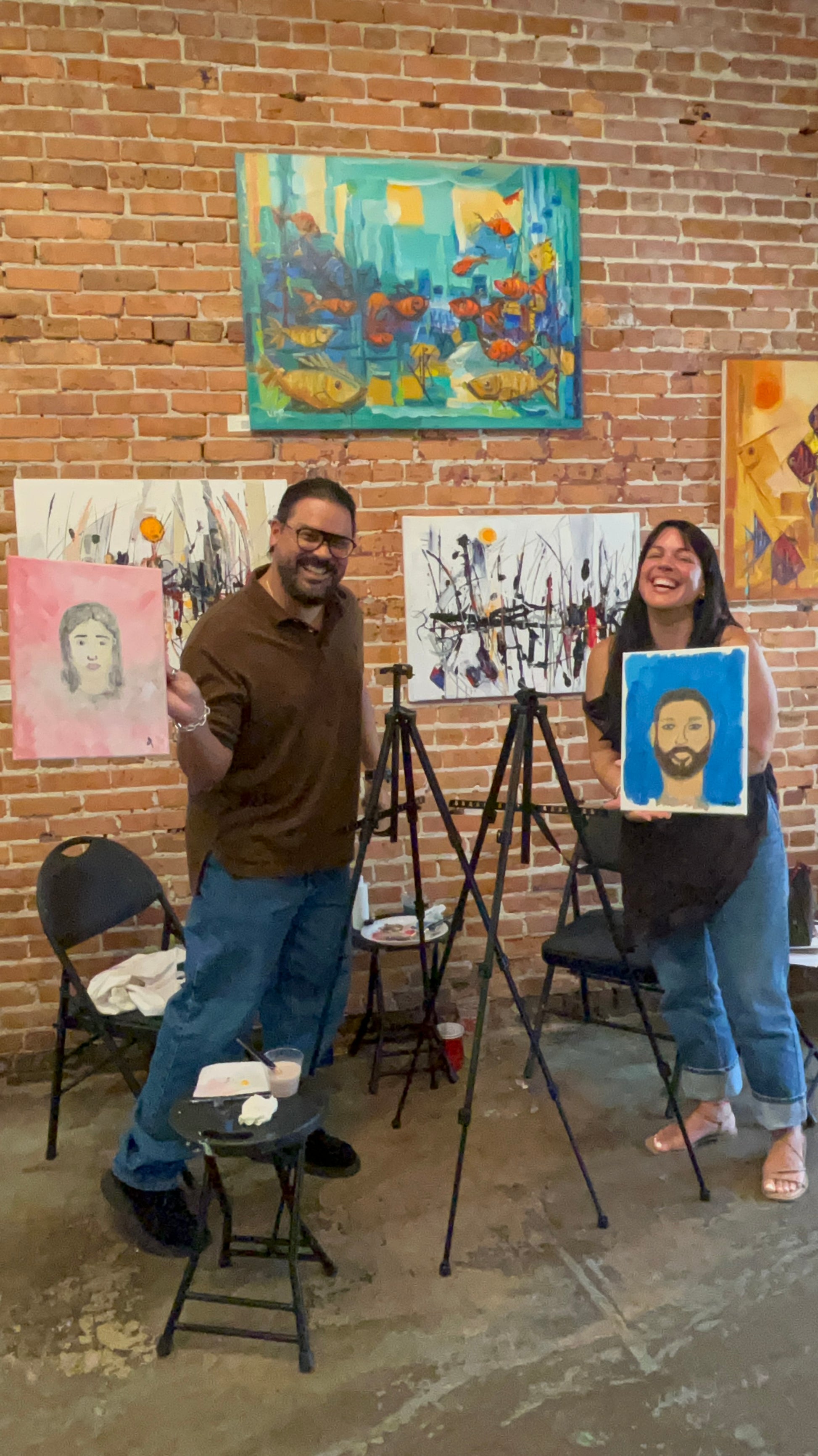 Couples proudly holding up the portrait artwork they painted of each other at the Marcolina's paint each other sip and paint event.