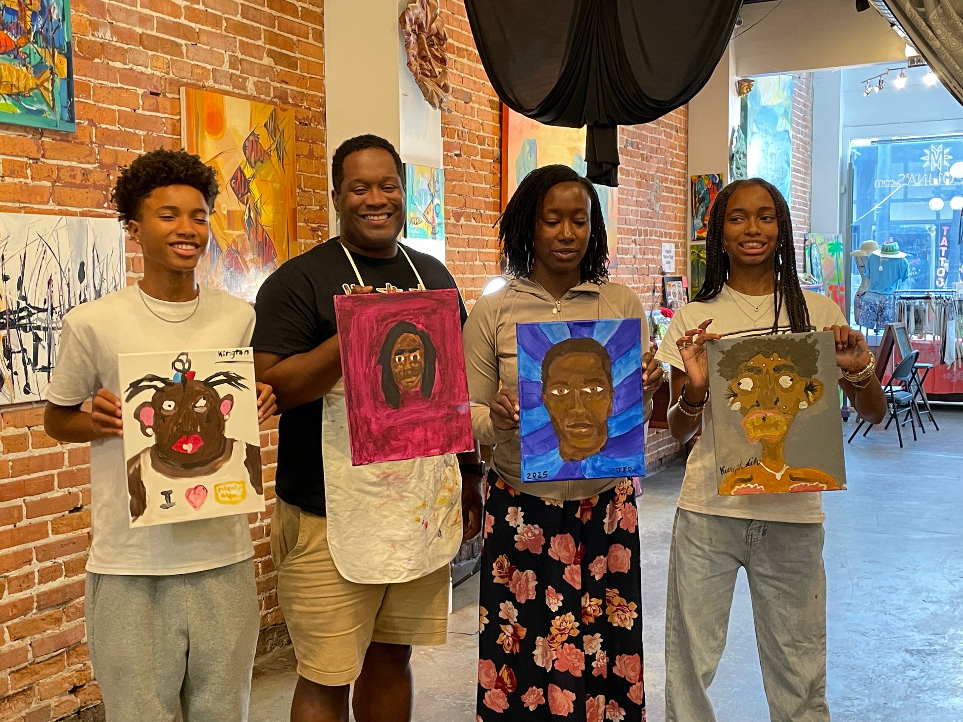 Family smiling and displaying the portrait paintings they created of one another during the sip and paint session at Marcolina's art gallery in Tampa.