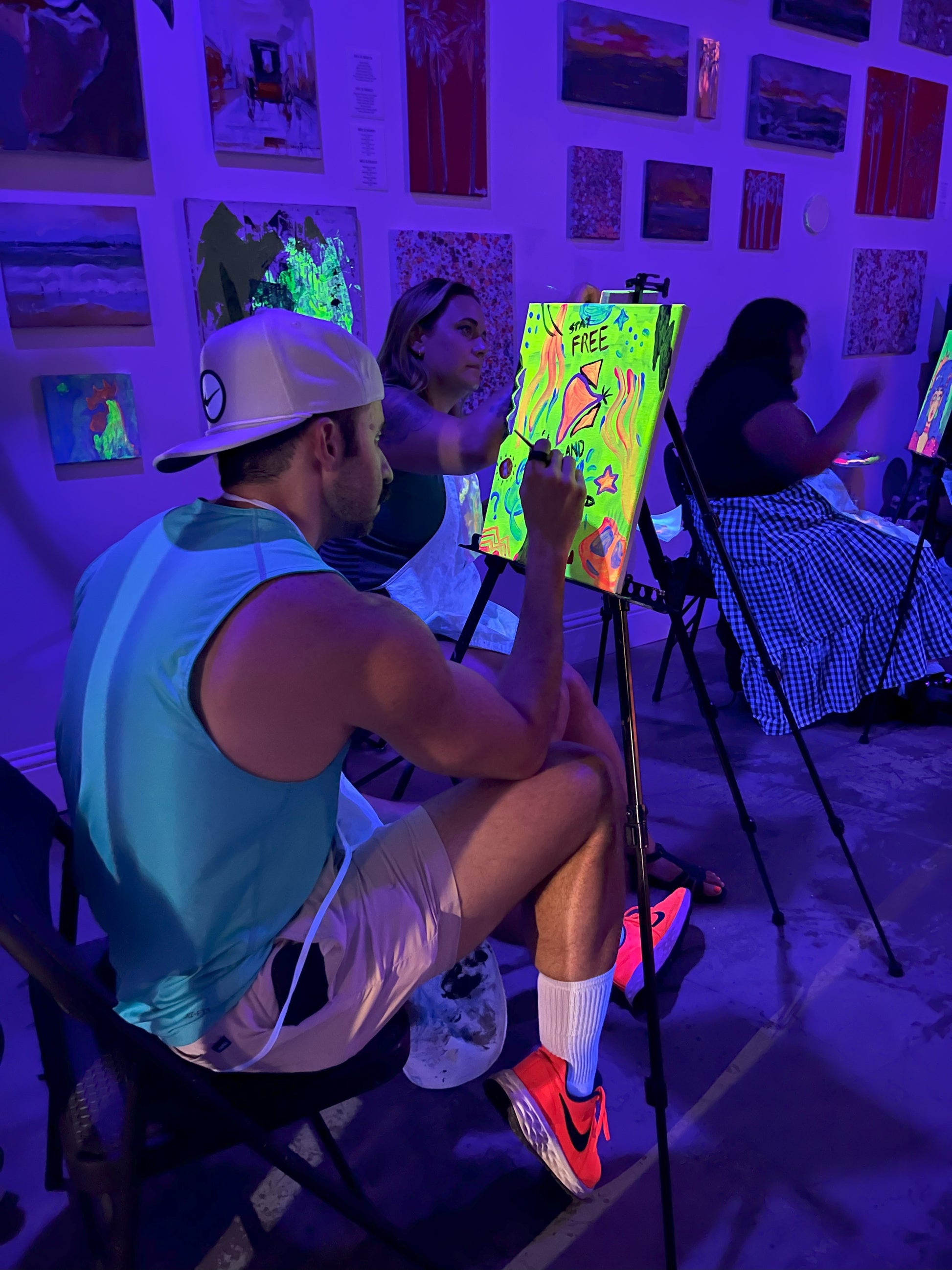 Guests painting glowing canvases under blacklights at Neon Nights BYOB sip and paint event at Marcolina's art gallery in Tampa.
