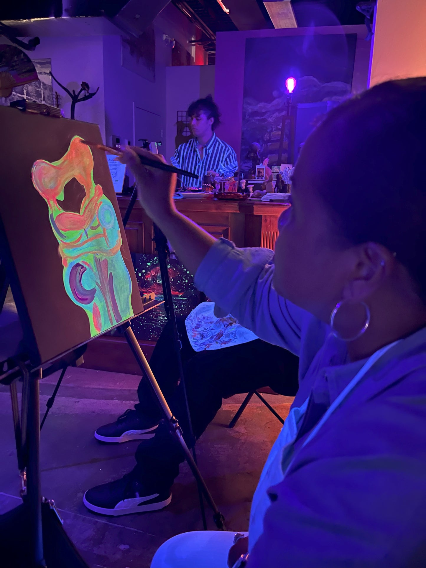Guest painting glowing canvases under blacklights at Neon Nights BYOB sip and paint event at Marcolina's art gallery in Tampa.
