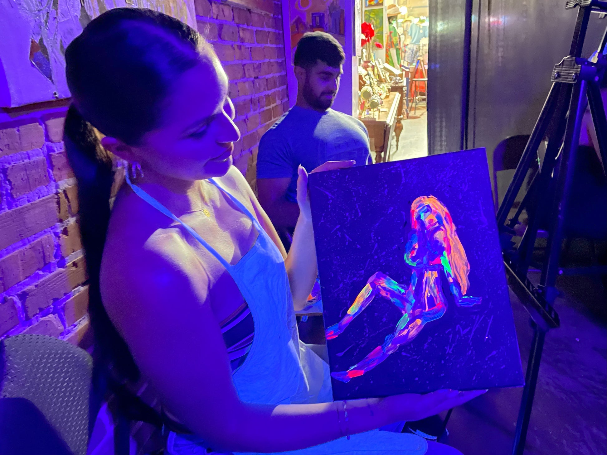 Guest proudly holding her neon paintings after a BYOB Neon Nights paint and sip session at Marcolina's art gallery in Tampa.