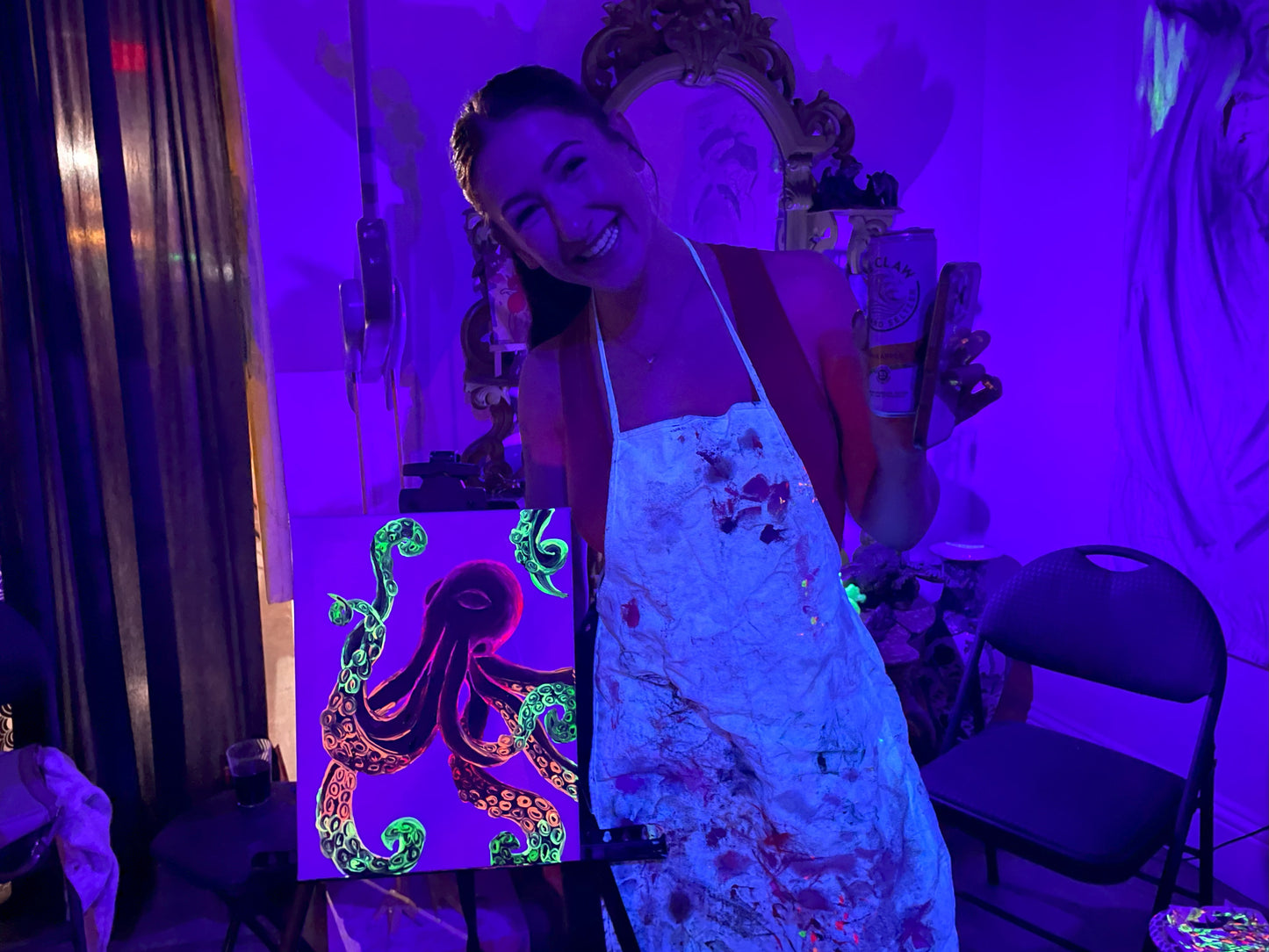Guest smiling while showing her neon portrait paintings at Neon Nights Sip & Paint party at Marcolina's art gallery in Tampa.